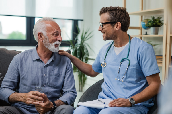 An older man speaking with his doctor in a comfortable setting. The doctor has his hand on the older gentleman's shoulder.