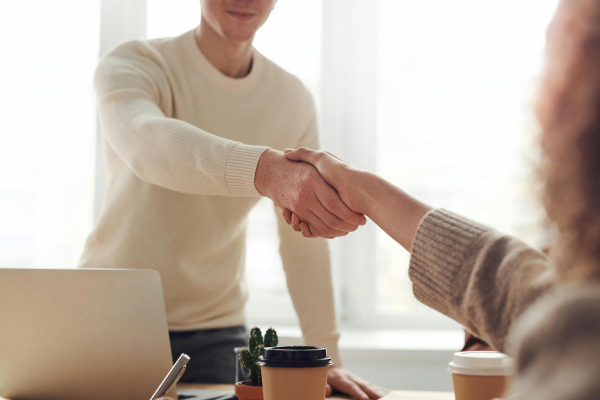Two people shaking hands over a desk and coffee cups