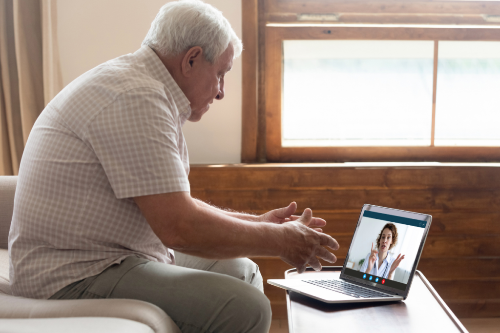 Older man sits on a couch talking to a woman on a laptop screen