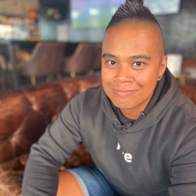 Man in his late 30's sits on a couch smilling at the camera.